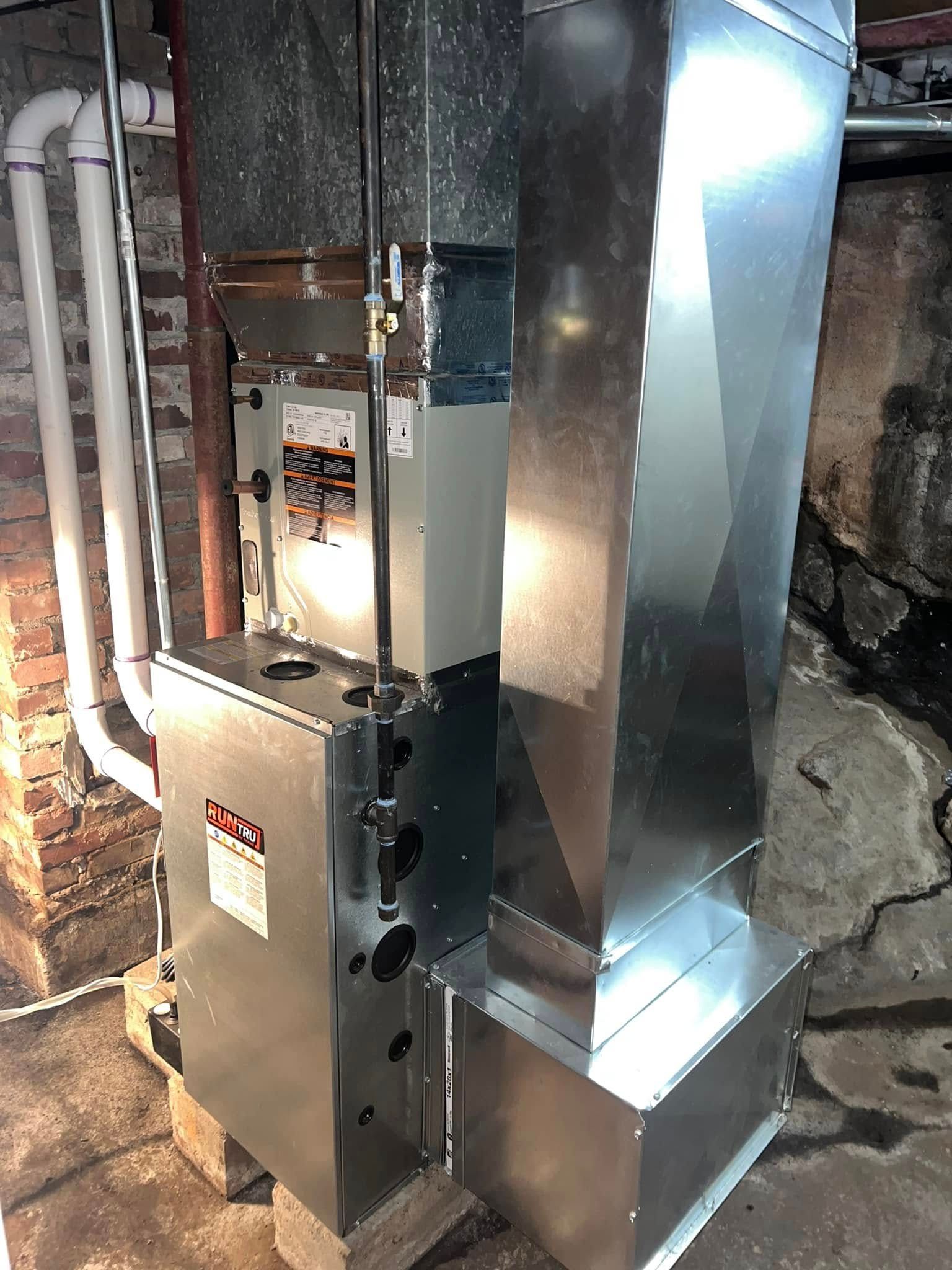 A stainless steel air conditioner is sitting in a basement next to a brick wall.