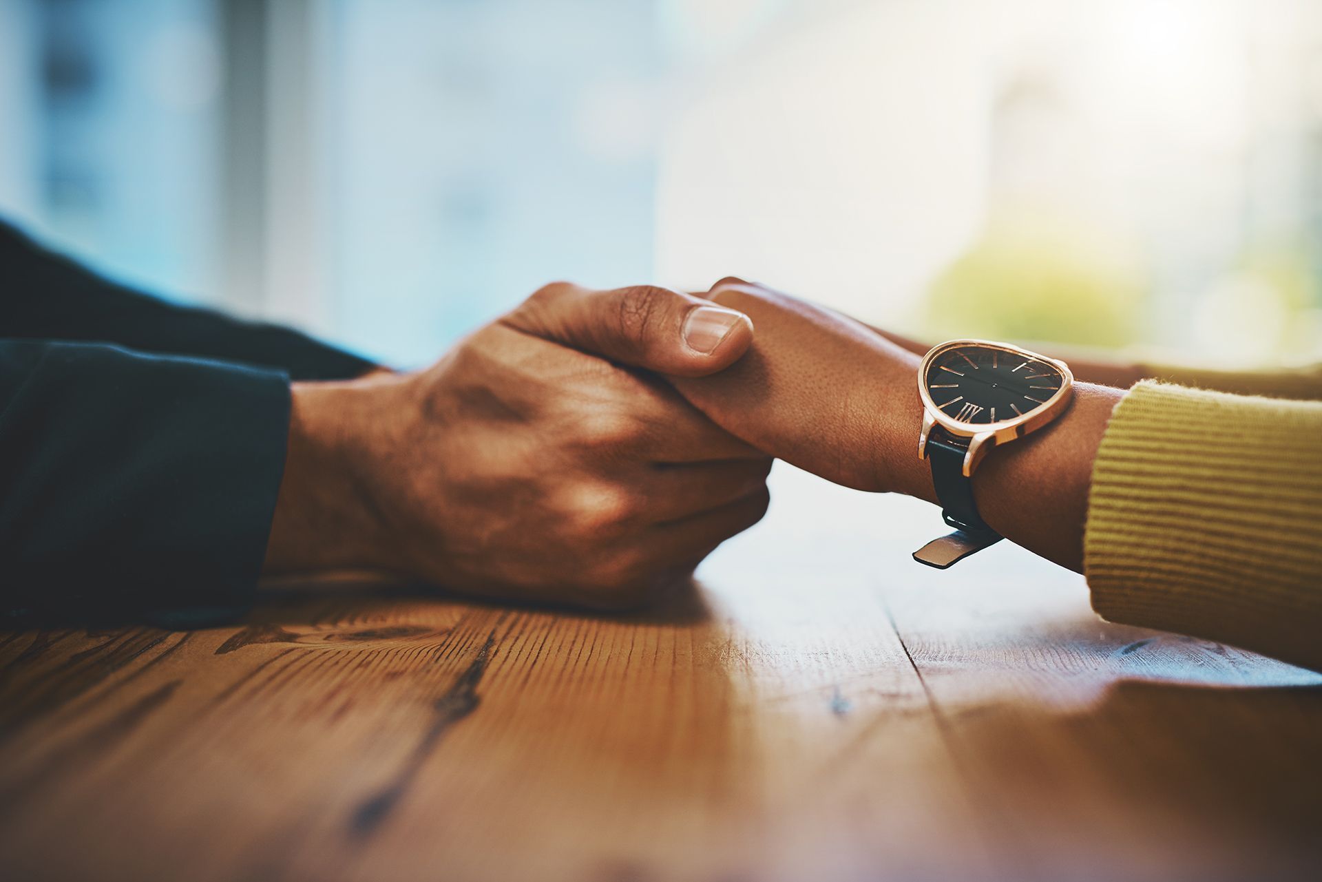 A man and a woman are holding hands over a wooden table.