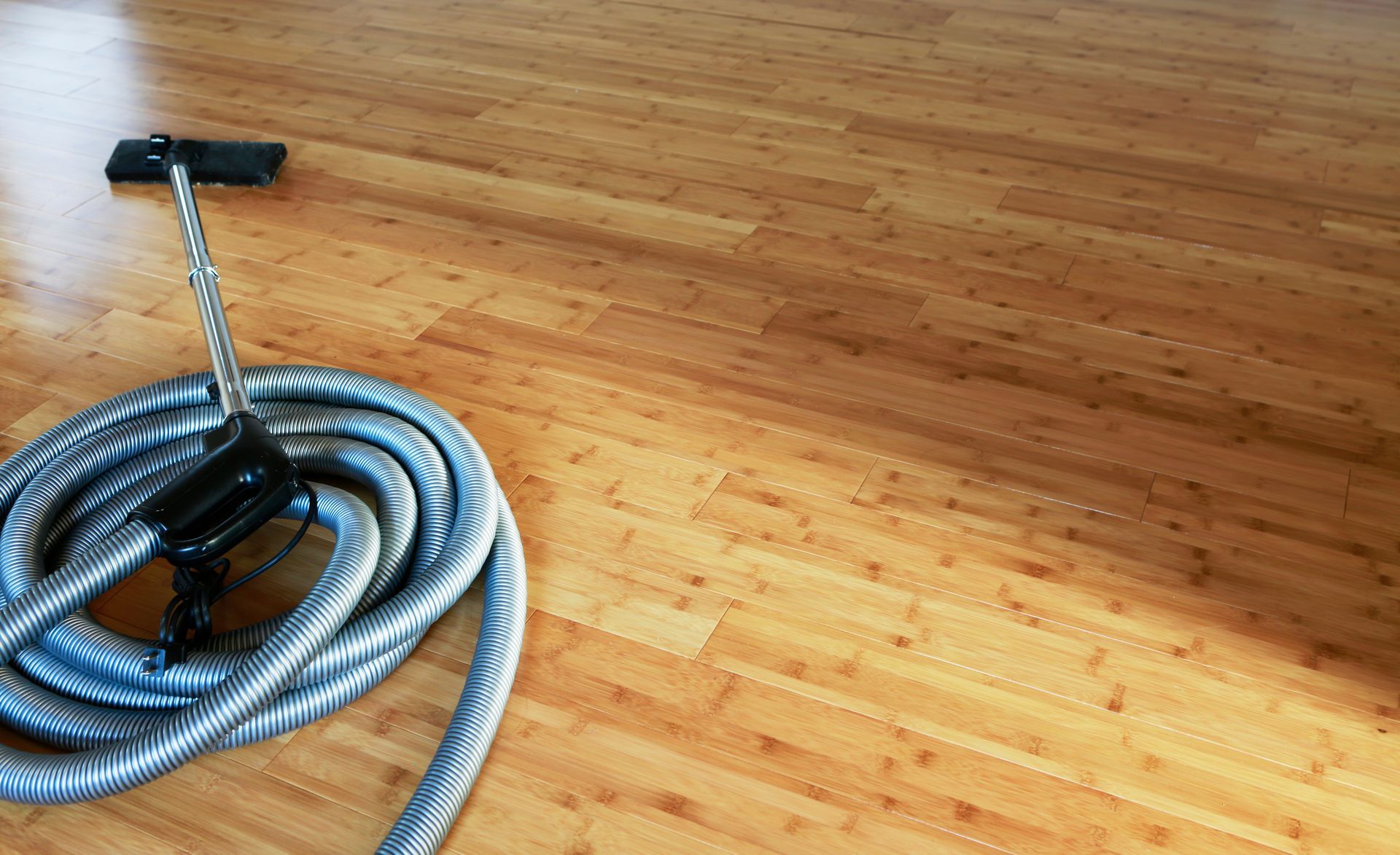 Vacuum hose with attachment coiled on a bamboo floor.