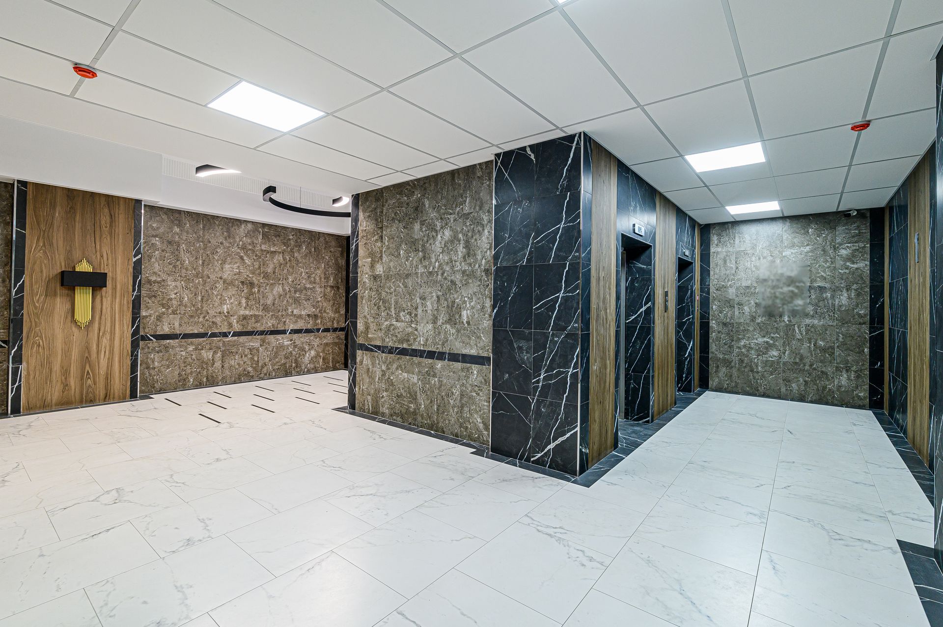 Elevator lobby with marble walls, wood accents, white tile floor, and recessed lighting.