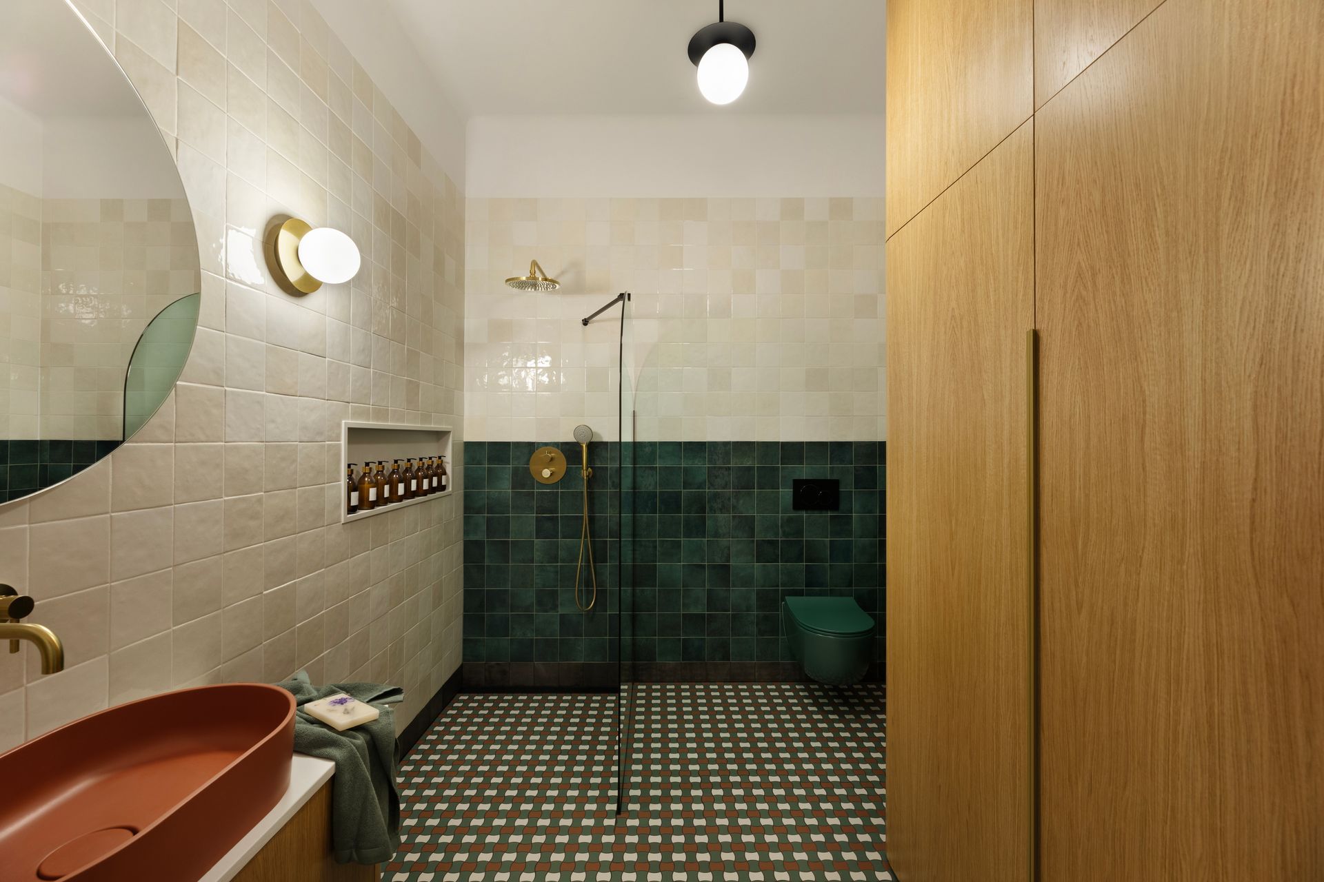 Bathroom with tan, green, and wood tones. Round mirror, vessel sink, and large wood storage unit.