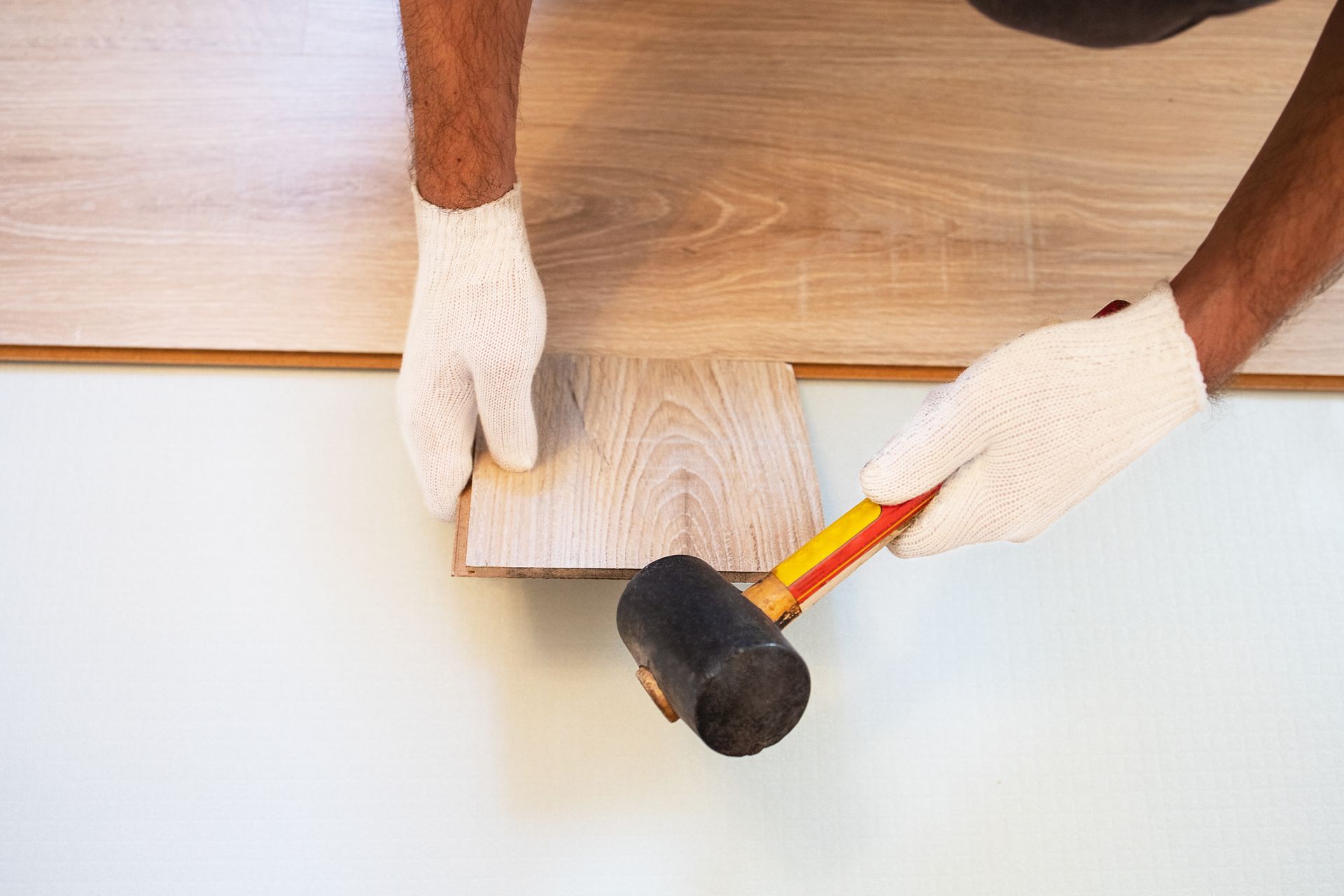 Person installing laminate flooring, using a mallet to tap a plank into place. Person installing laminate flooring, using a mallet to tap a plank into place.