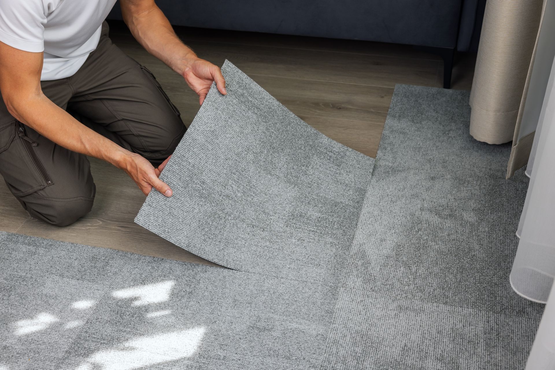 Person installing gray carpet tiles on a floor.