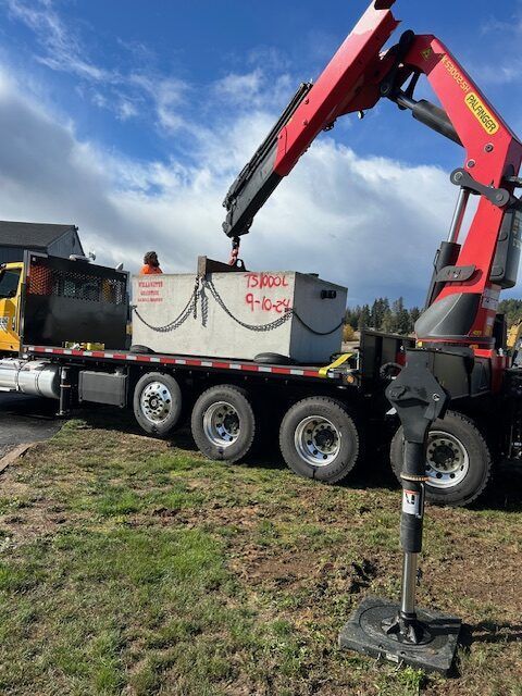 A crane is lifting a large concrete block on a flatbed truck.