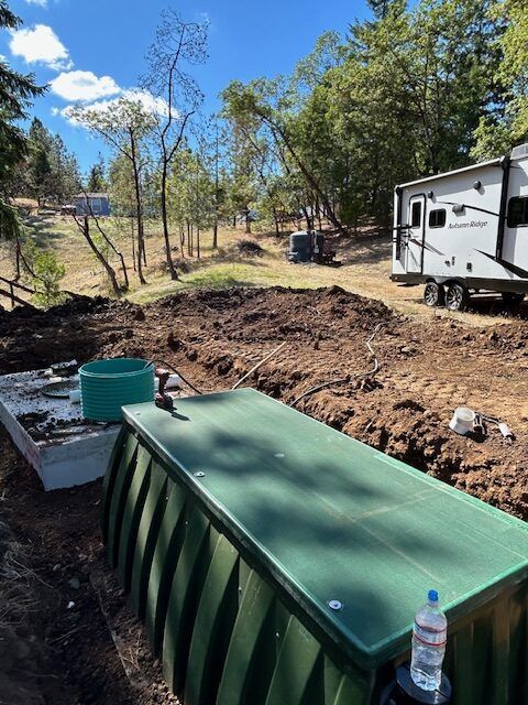 A green tank is sitting in the dirt next to a trailer.