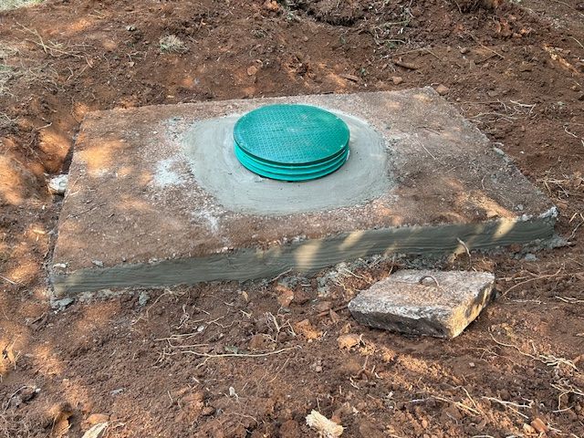 A green lid is sitting on top of a concrete block in the dirt.
