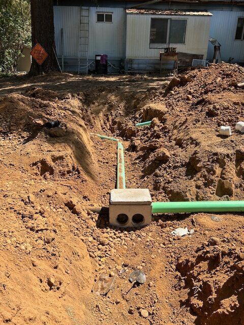 A green pipe is being installed in the dirt in front of a house.