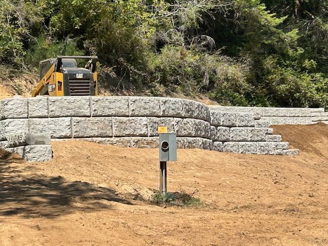 A bulldozer is driving down a dirt road next to a stone wall.
