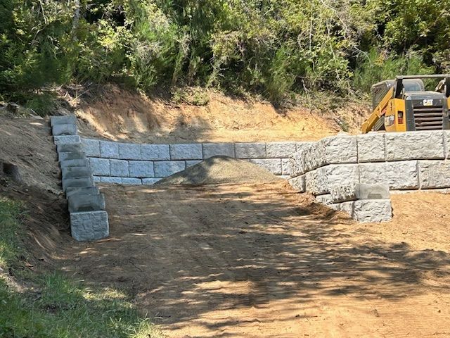 A bulldozer is driving down a dirt road next to a stone wall.