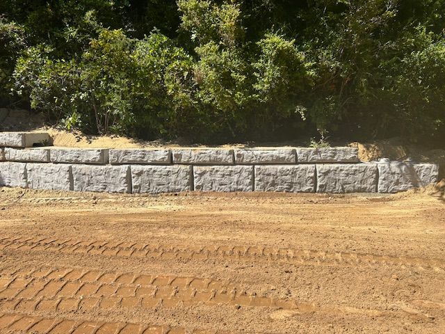 A large stone wall is sitting in the middle of a dirt field.