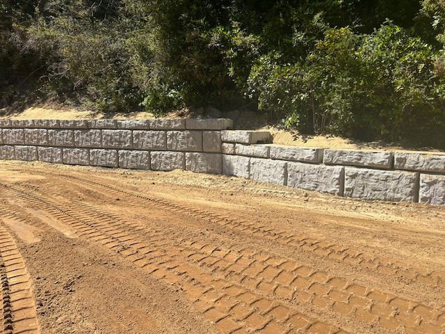 A large stone wall is being built on the side of a dirt road.