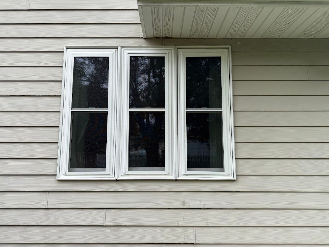 Three vertical windows with white frames on a beige house exterior.
