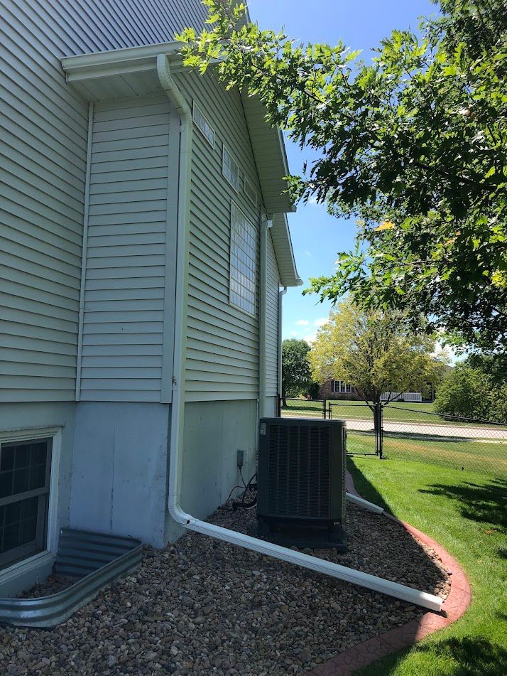 Side view of a house with white siding, gutters, and an air conditioning unit; sunny outdoor setting.