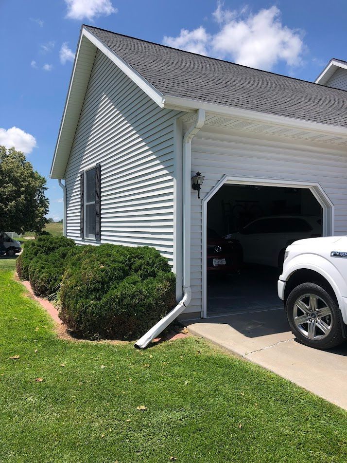 Garage with open door, light blue siding, white truck parked in front, green lawn, cloudy sky.