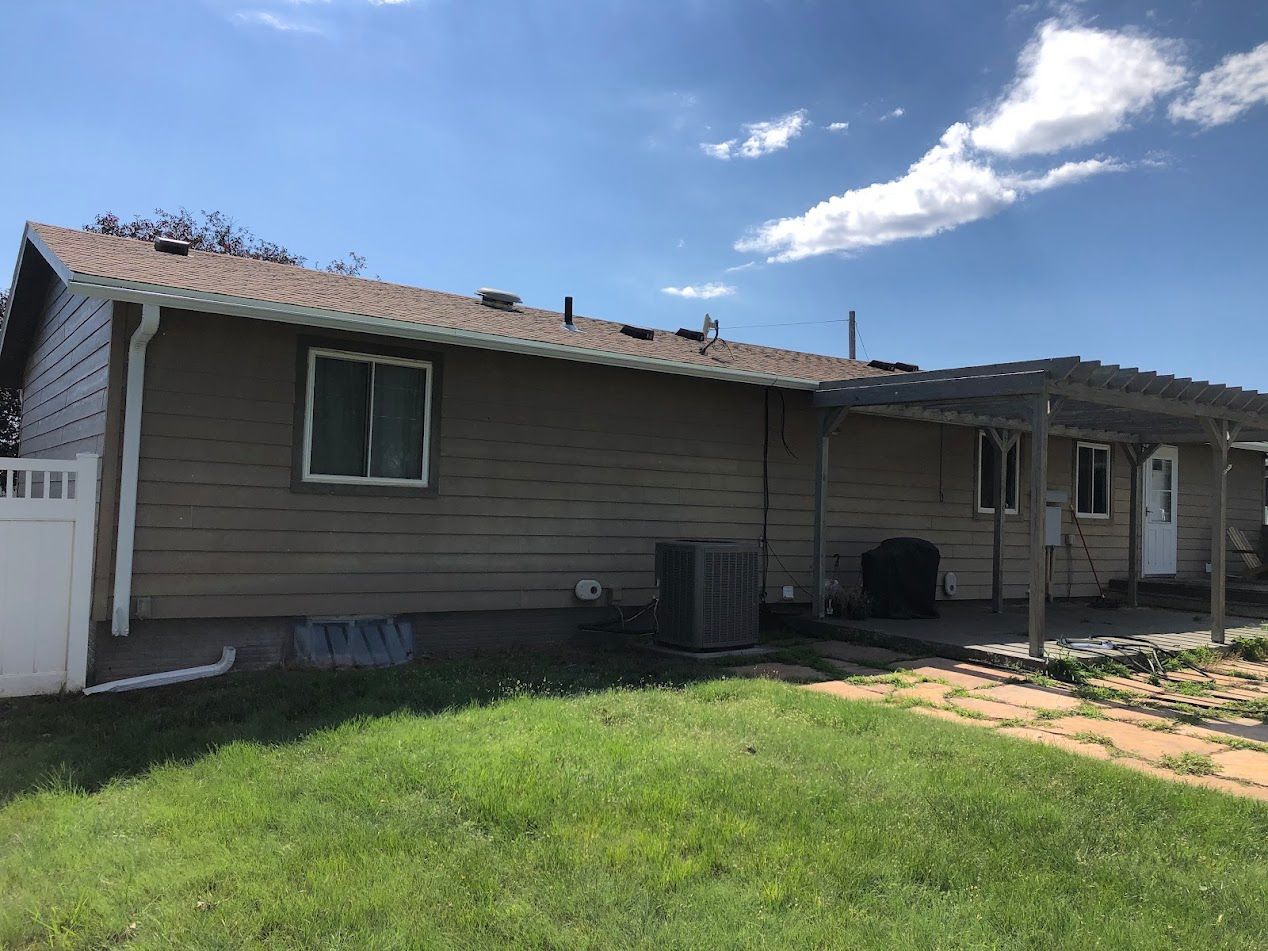 Tan house with white trim, green grass, and a blue sky with clouds.