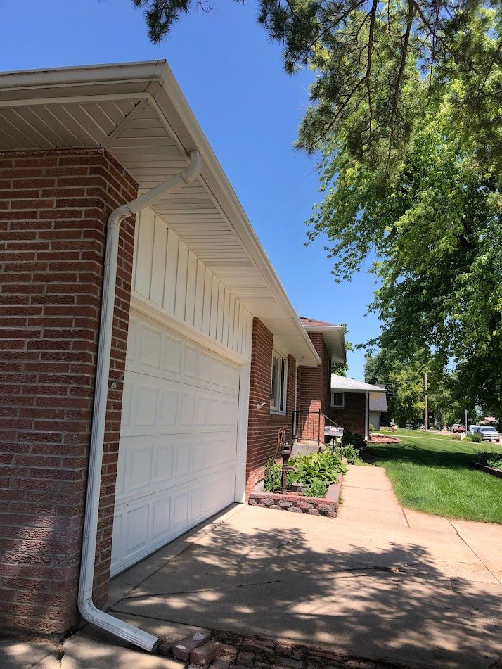 Brick house with white garage door and trim, white gutters. Sunny day.