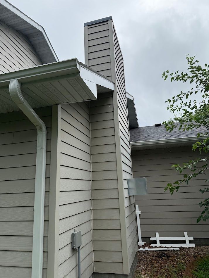 Exterior view of a house with a tall chimney, beige siding, white trim, and a cloudy sky.