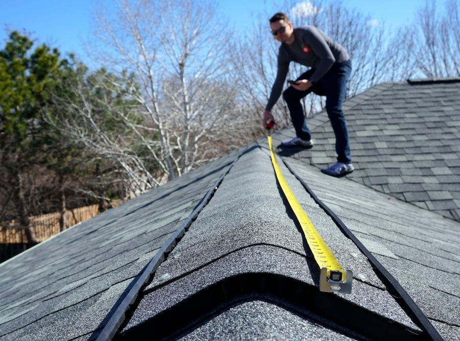 A man is measuring a roof with a tape measure.