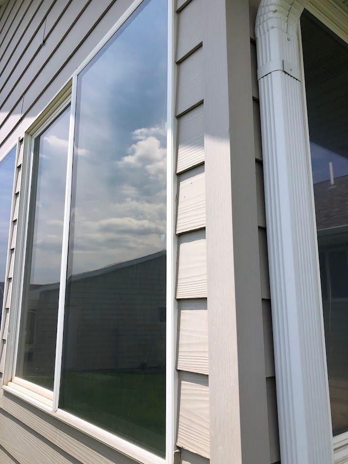 Corner of a building with large windows reflecting sky and siding. White trim and gutter.