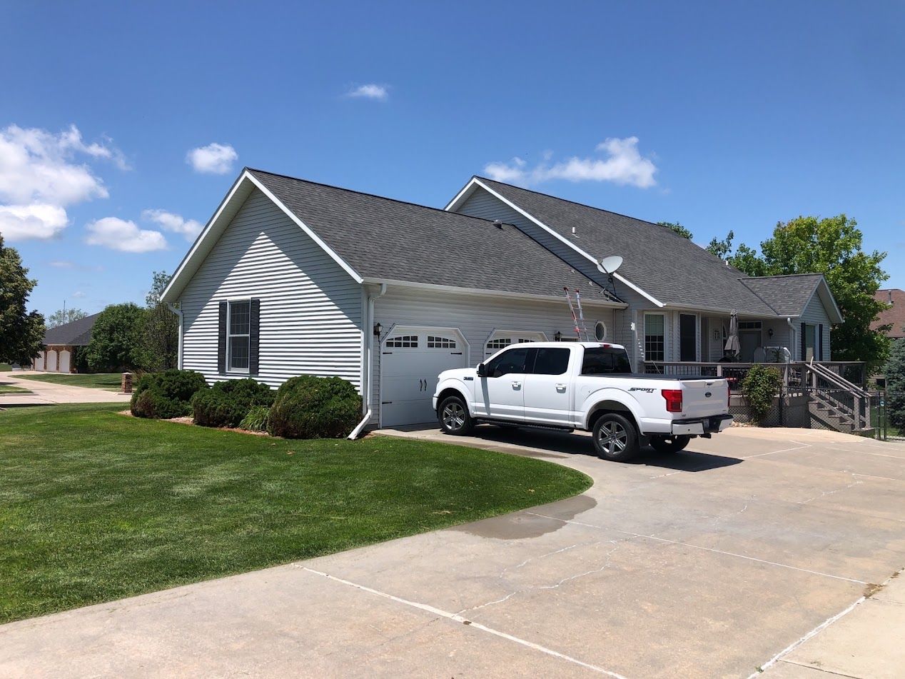 White pickup truck parked in front of a white house with a gray roof and green lawn on a sunny day.