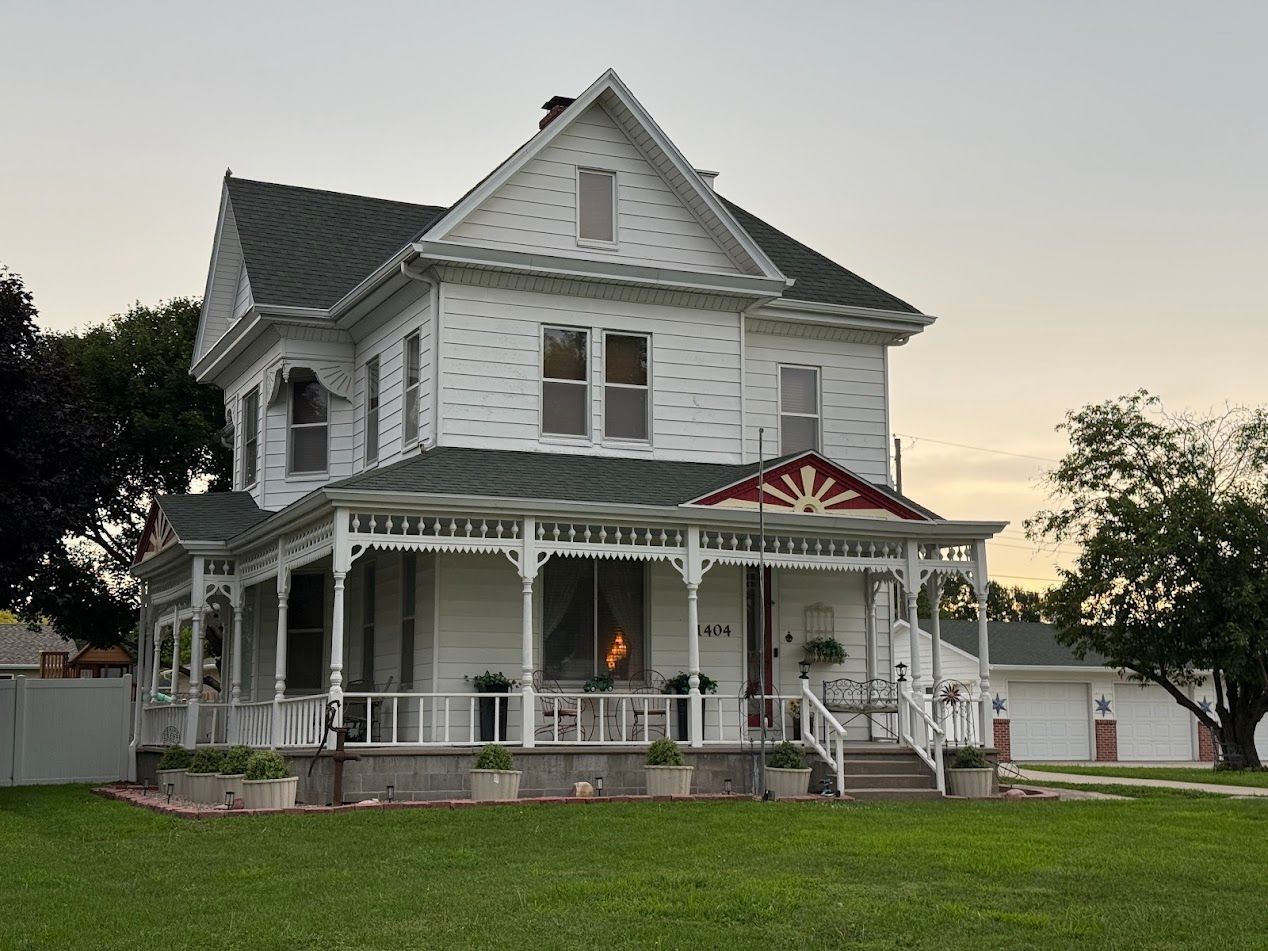 White Victorian house with porch, green roof, and lawn under a cloudy sky.