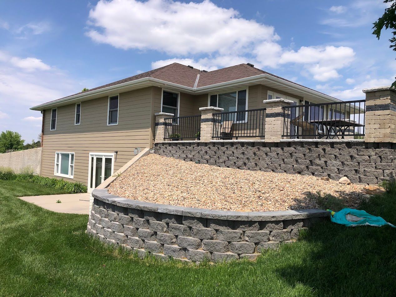 Beige house with a retaining wall, deck, and sloping yard on a sunny day.