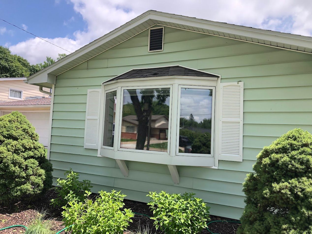 Light green house with a bay window, white shutters, and a garden.