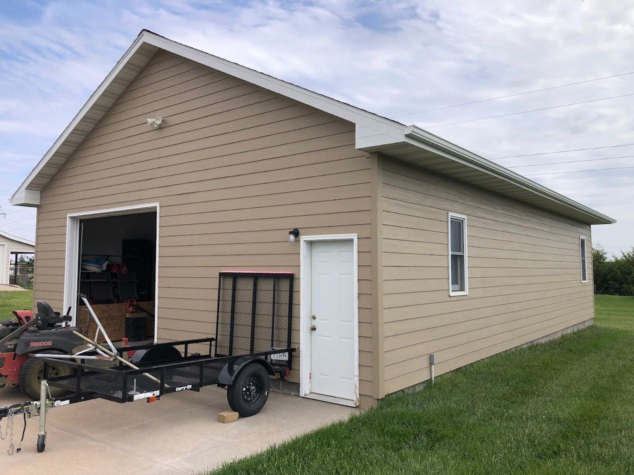 Tan sided garage with open door, small door, window and lawn care equipment on the concrete.