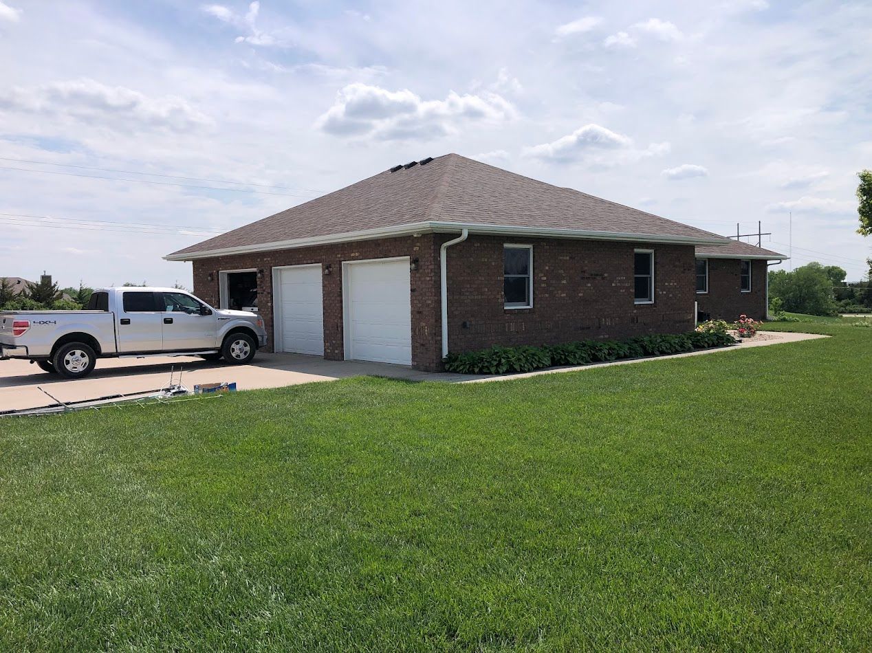 Brown brick house with two-car garage and pickup truck parked in front; green grass surrounds.