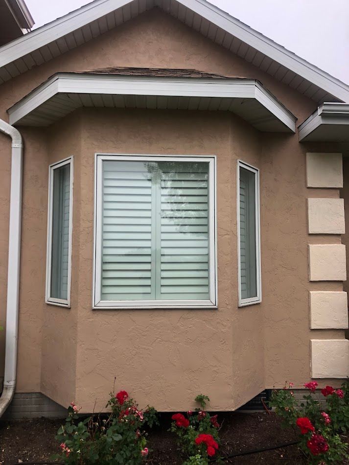 Beige house exterior with angled bay window, white trim, and red rose bushes.