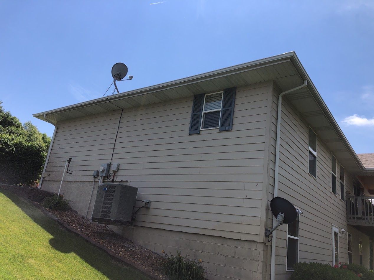 Beige two-story building with satellite dishes on a grassy hillside under a blue sky.