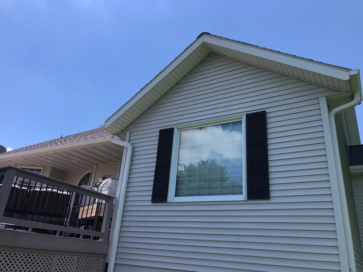 Exterior of a house with white siding, black shutters, and a deck under a clear blue sky.