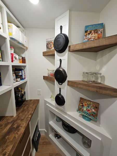 Pantry interior with white shelves and a dark countertop. Cast iron pans hang on a wall.