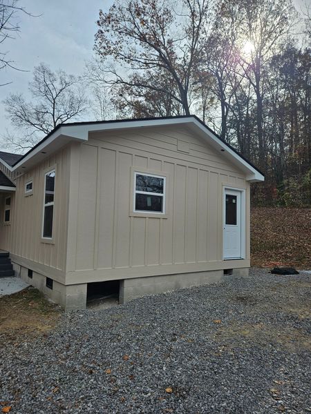 Beige-sided building with black roof, white trim, and window. Door visible. Cloudy day.