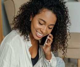 A woman is smiling while talking on a cell phone.