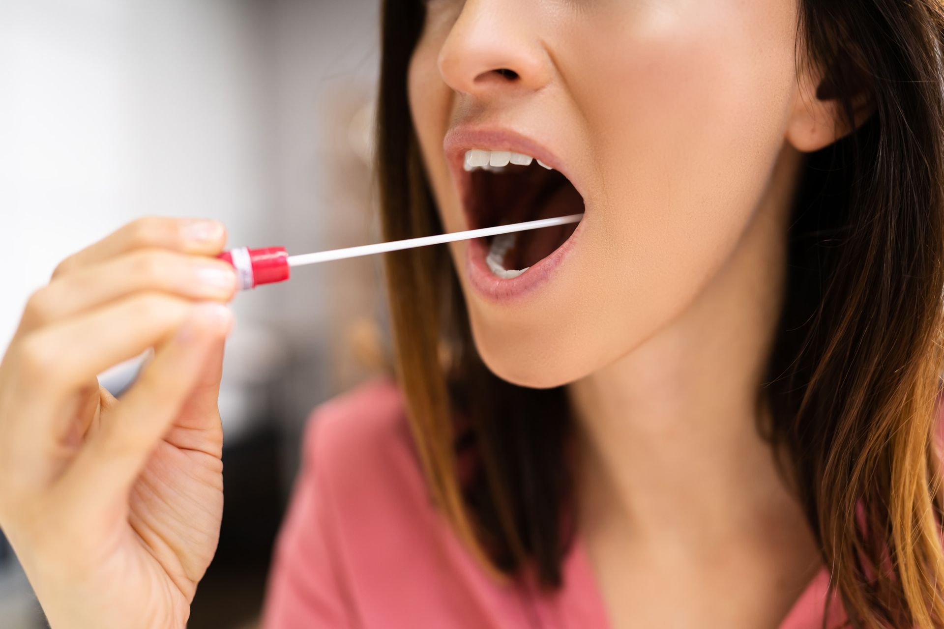 A woman is taking a sample from her mouth with a swab.