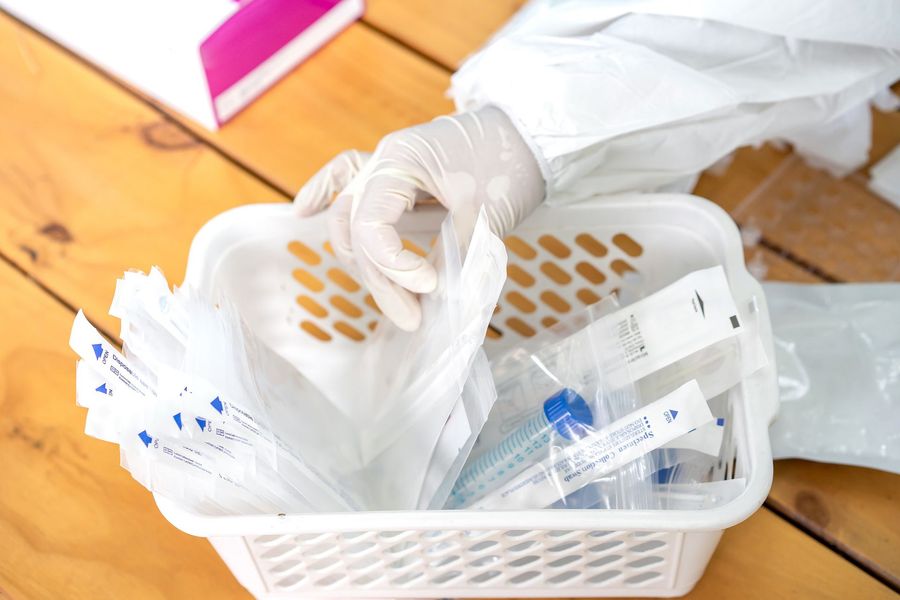 A person wearing gloves is holding a plastic bag over a basket filled with plastic bags.