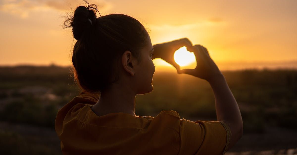 Women viewing sunset expressing a heart with her hands.
