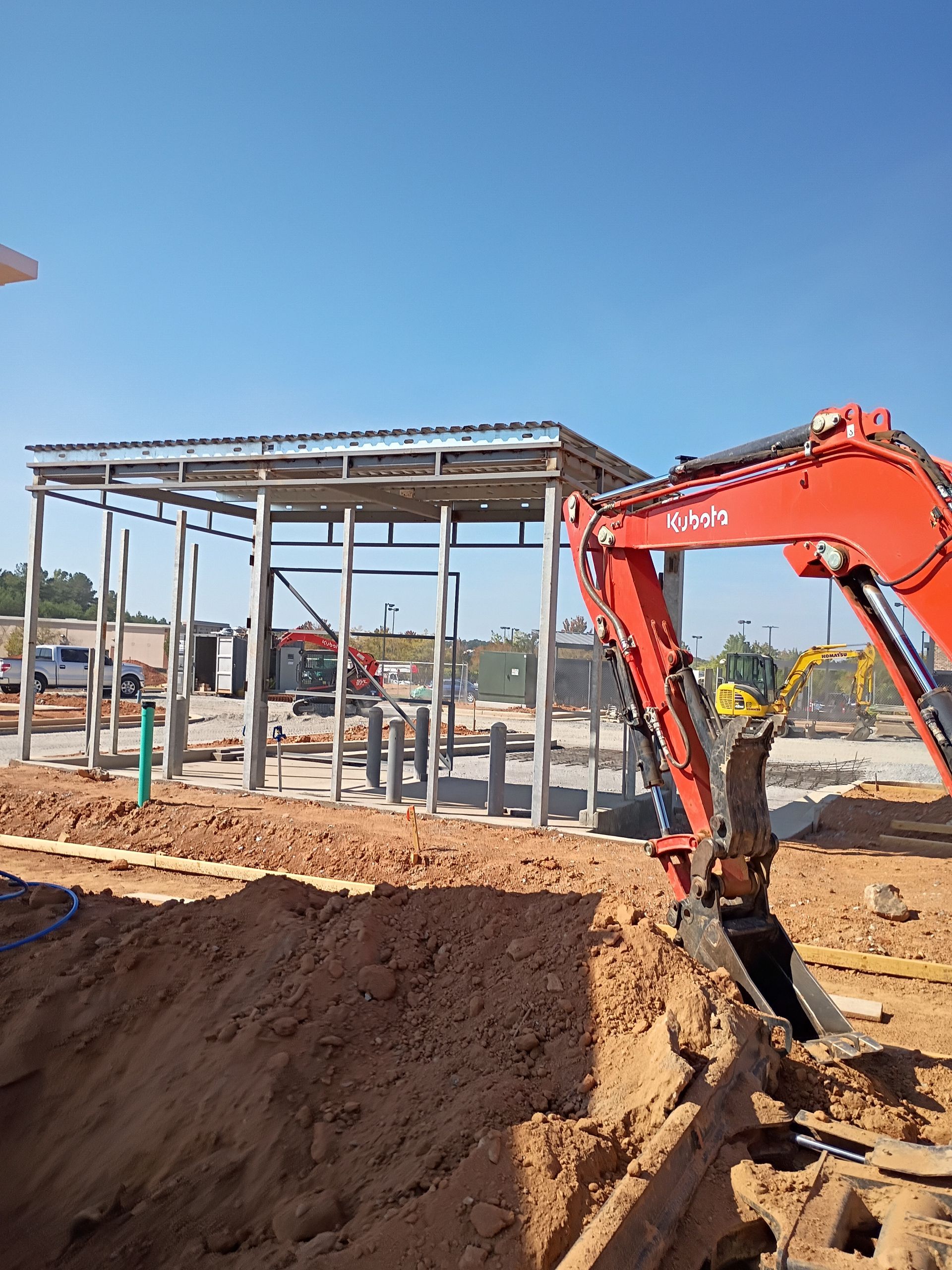 Orange excavator digging near a steel-frame building site under a clear blue sky