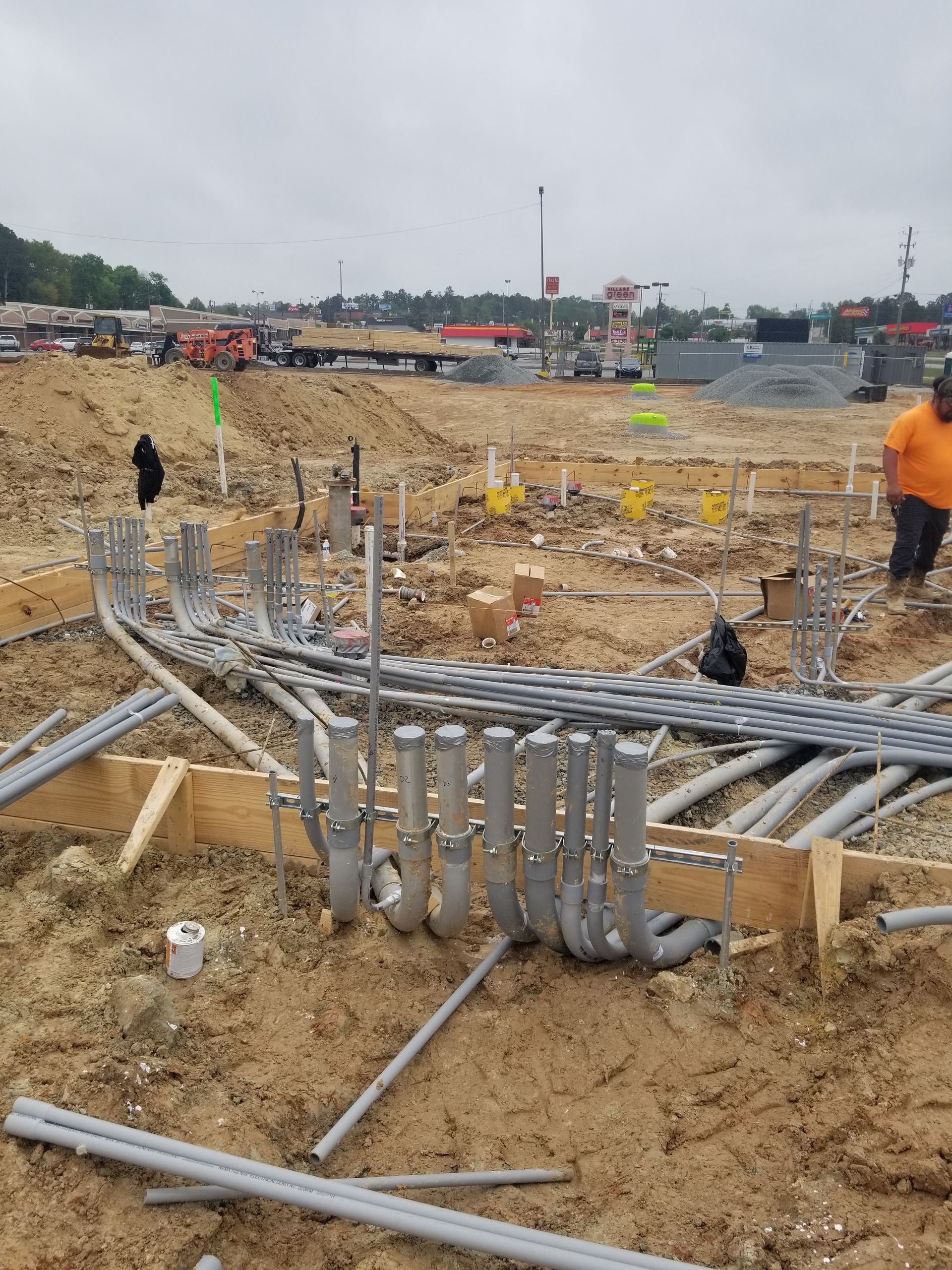 Construction site with trenches, pipes, and workers in orange vests on sandy ground