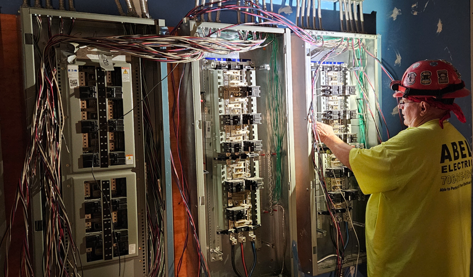 Worker inspecting electrical control panels with exposed wiring in a utility room