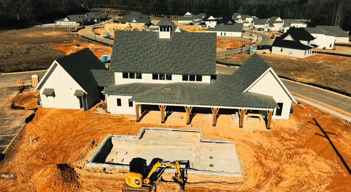 New house under construction with roof, porch, and excavator on a cleared lot