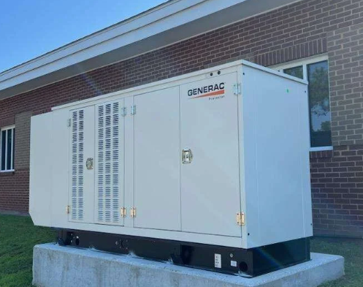 White industrial generator unit beside a brick building on a concrete pad outdoors