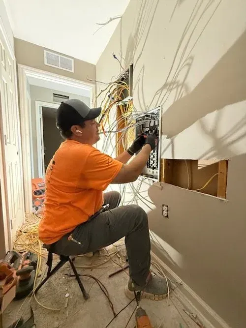Electrician in orange shirt wiring an open wall box in a hallway renovation