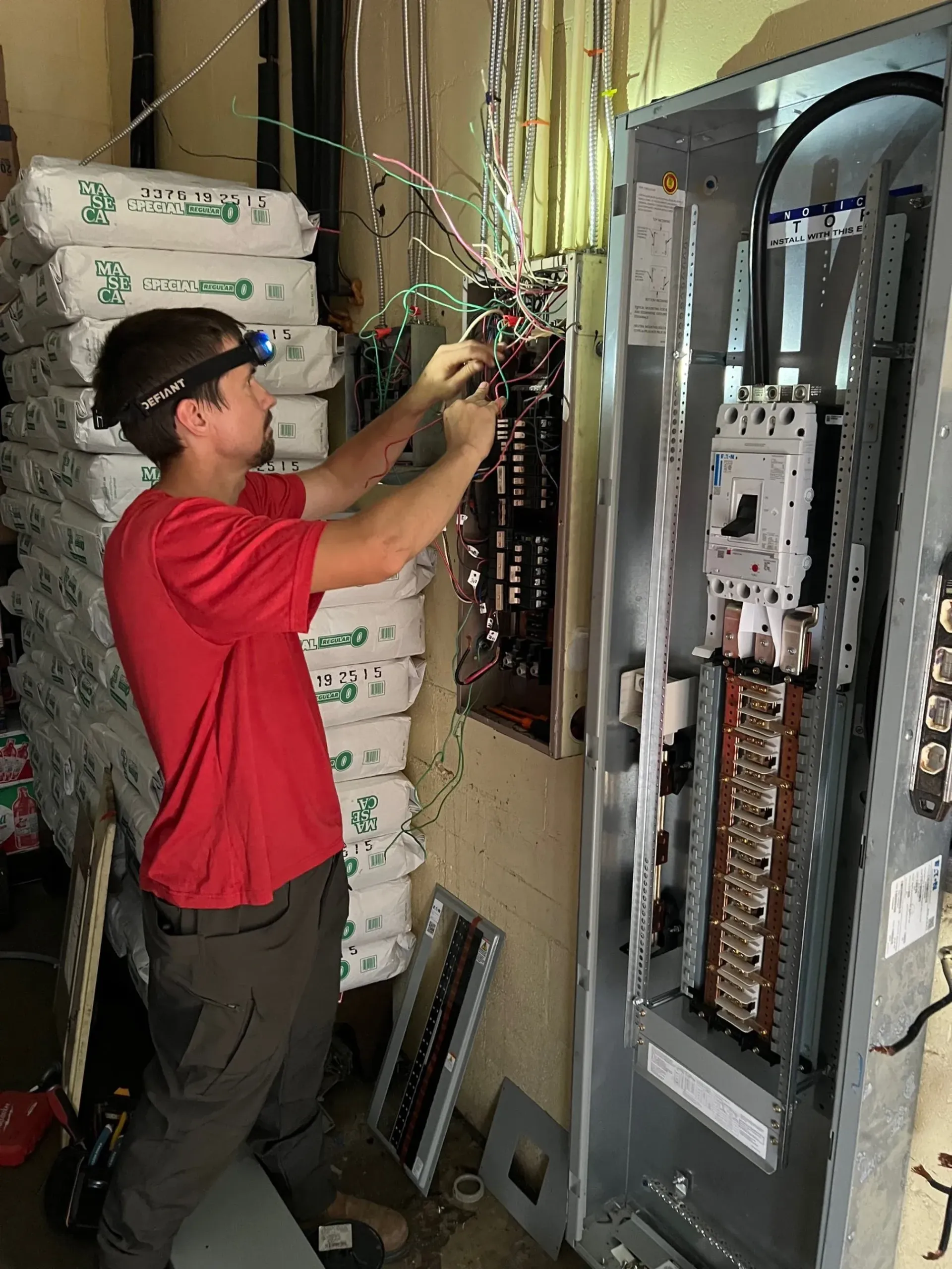Technician in red shirt wiring an electrical panel in a utility room