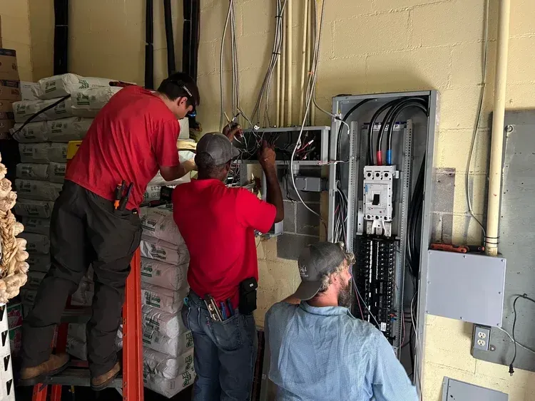 Three workers wiring an electrical panel in a utility room
