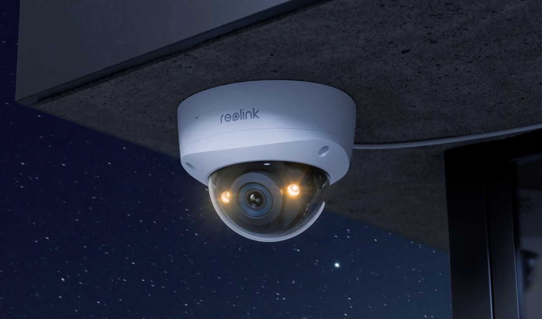 Ceiling-mounted security camera with a dome lens and two lights, under an overhang at night