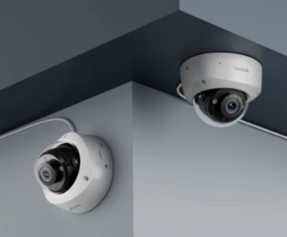 Two white dome security cameras mounted on a gray corner ceiling, one facing outward and one angled down.