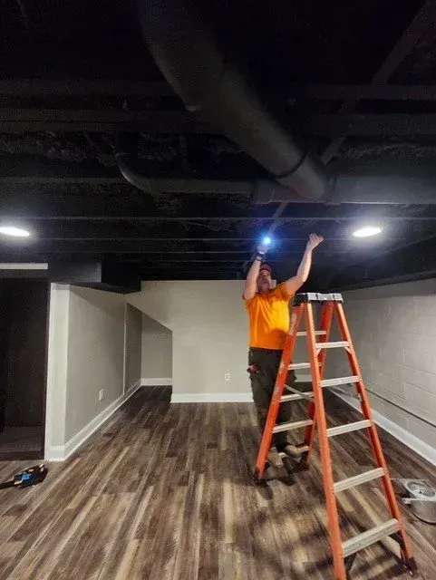Person on a ladder inspecting the black ceiling in a vacant room with wood floors