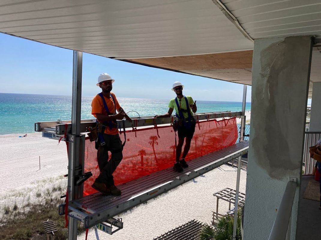 two construction workers are standing on a balcony overlooking the ocean .